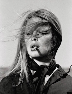 Brigitte Bardot by Terry O'Neill, black and white portrait of the actress in black blouse and scarf, hair blowing in the wind, smoking a cigarette