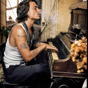 Johnny Depp by Mark Seliger, the actor in a white tank top in side profile playing the piano while smoking