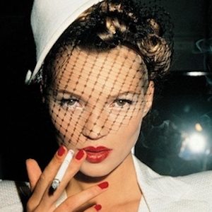 Kate Moss Smoking by Roxanne Lowit, portrait of the model in white suit and hat with a veil, wearing red nailpolish and lipstick, holding a cigarette