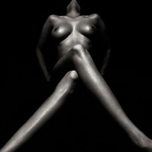 Nude 132 by Andreas H. Bitesnich, black and white photo of a nude female model in high contrast lighting sitting crossed legged