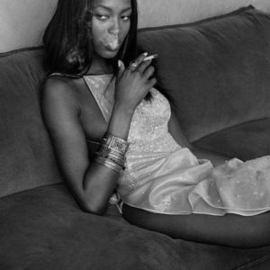 Naomi Campbell Smoking, Morocco by Albert Watson, black-and-white vintage fine art photography showing the supermodel with a cigarette sitting on a sofa wearing a white sequin dress