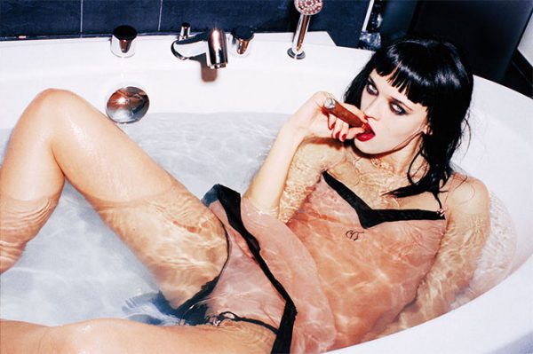 Anna Nass by Ellen von Unwerth, model in pink and black dessous and smokey eyes lying in a bathtub and smoking a cigar