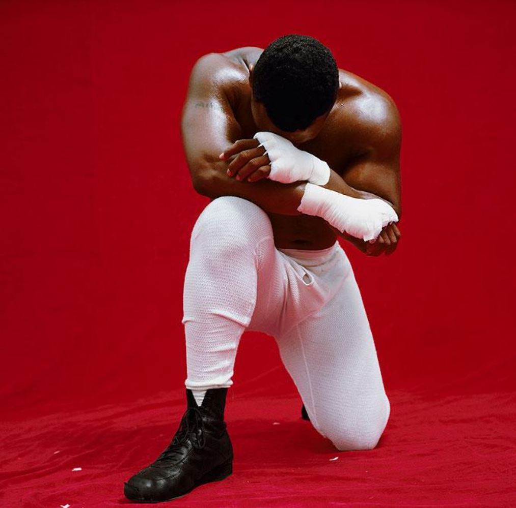 Mike Tyson by Michel Comte, the boxer in white pants and handwraps kneeling in front of red background