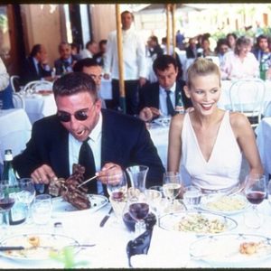 Claudia Having Lunch in Rome. 1990 by Arthur Elgort, the model in a white top sitting at a lunchtable with men in suits