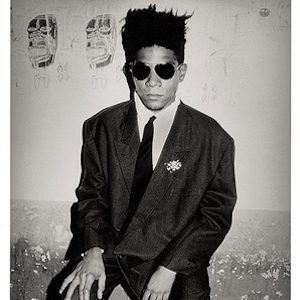 Jean-Michel Basquiat, Palladium, NYC. 1985 by Roxanne Lowit, portrait of the artist in suit and sunglasses holding a cigarette