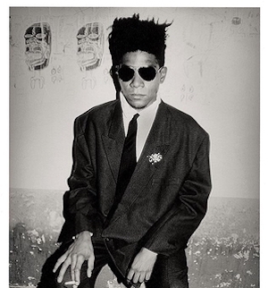 Jean-Michel Basquiat, Palladium, NYC. 1985 by Roxanne Lowit, portrait of the artist in suit and sunglasses holding a cigarette