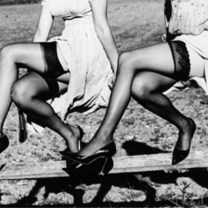 legshow 2 by Ellen von Unwerth, two models in black stockings and heels sitting i a wooden fence, their legs crossed