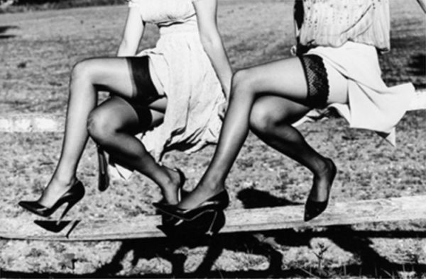 legshow 2 by Ellen von Unwerth, two models in black stockings and heels sitting i a wooden fence, their legs crossed