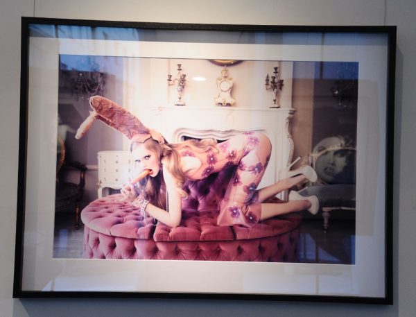 Little Beast by Ellen von Unwerth, model in pink latex flowerdress and bunnyear headpiece, kneeling on a sofa and eating a carrot, framed black