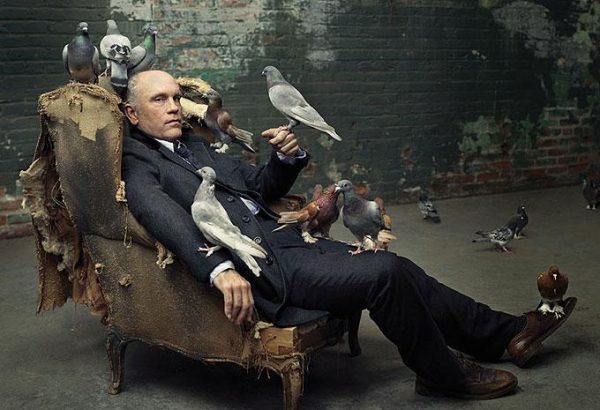john malkovich with doves by Mark Seliger, the actor in a suit sitting in a broken armchair, surrounded by doves