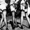 Leg Show by Ellen von Unwerth, three models in black stockings and heels pulling their skirts up
