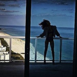 Recap by David Drebin, model in fur jacket standing on a balkony, beach and ocean in the background