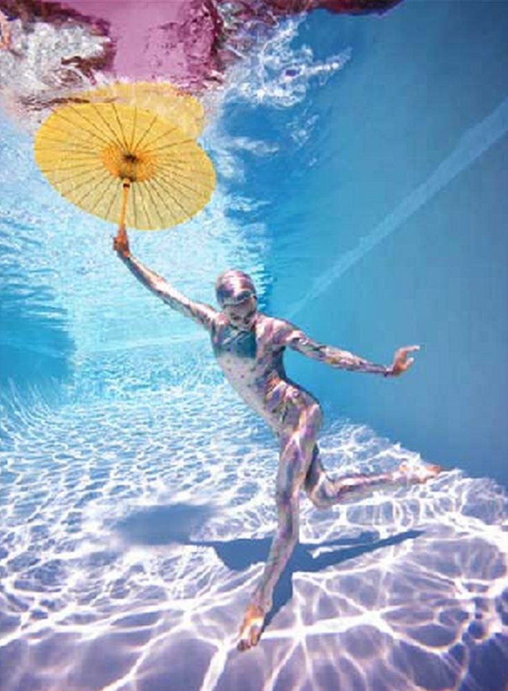 Underwater Study #2778 by Howard Schatz, model in pastel leotard and cap, holding a yellow umbrella underwater in a pool