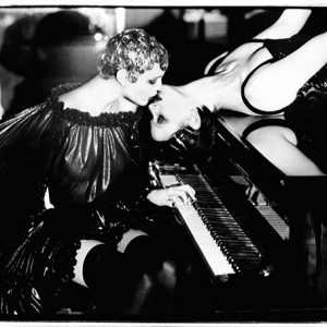 Sonate by Ellen von Unwerth, model in transparent dress and short blonde hair sitting at the piano, kissing another model who is lying on the piano
