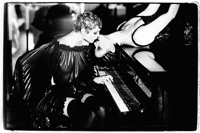 Sonate by Ellen von Unwerth, model in transparent dress and short blonde hair sitting at the piano, kissing another model who is lying on the piano