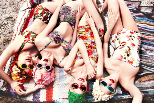 Freshly Bloomed by Ellen von Unwerth, four models in vintage bathing suits and bikinis in flowerprint with matching caps and sunglasses lying on a towel at the beach