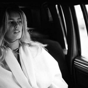 Claudia Schiffer by Antoine Verglas, portrait of the model i a white blouse sitting in a car, looking out the window