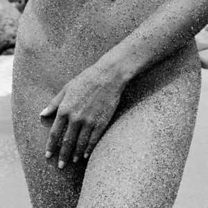 Petra Grand Fond, Shell Beach. 2015, nude model covered in sand lying on the ground crouched together, closeup of nude models hips, covered in sand, covering herself with her hand