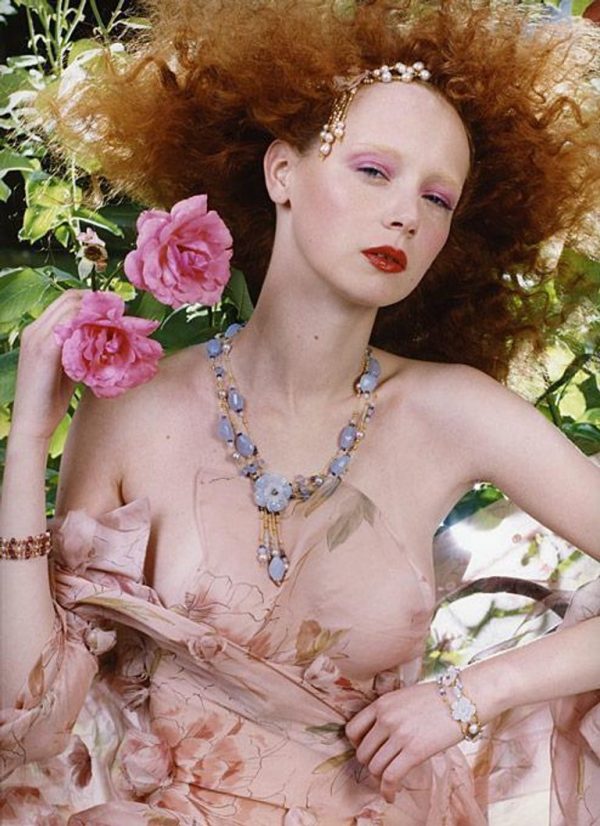 Red Hair 2 by Iris Brosch, portrait of a model with curly red hair wearing transparent flower fabric and holding two pink flowers