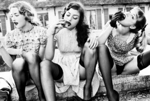 peaches by ellen von unwerth, three model in retro dresses and black stockings sitting on the curb, eating peaches