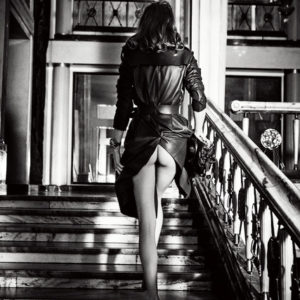 Undercover for VOGUE POLAND by Elen von Unwerth, model in trenchcoat with exposed butt walking up a marble staircase