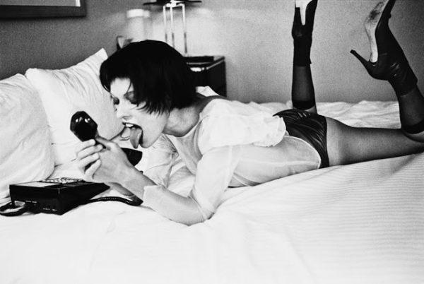 TELEPHONE SEX New York 1997, from the fräulein Series by Ellen von Unwerth, model in white blouse and black tights lying on a hotel bed, licking a telephone