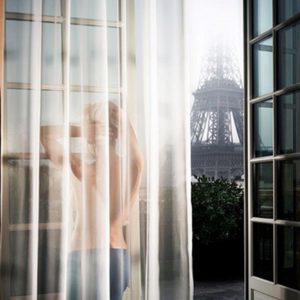 Girls in Paris by David Drebin, seminude model holding up her hair behind a curtain, the eiffeltower outside the window