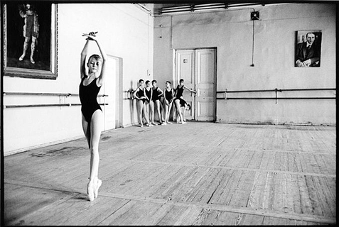 Olga by Arthur Elgort, ballerinas in black leotards, one on pointe in the front, the rest of the group aiting in a corner