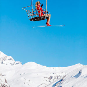Ski Patrol by Tony Kelly, model in red jacket and ski glued to her red heels in a chairlift obove snowy mountains