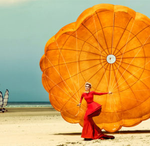 Nadja III by Kristian Schuller, Nadja Auermann in red dress with orange parachute on the beach