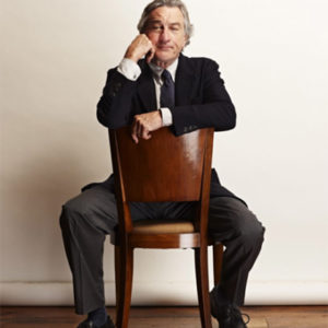 Robert De Niro on Chair by Nigel Parry, portrait of the actor in a suit sitting on a wooden chair the wrong way round