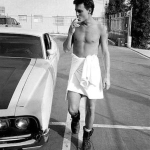 Johnny Depp Hollywood by Sante D'Orazio, the actor walking thrugh a car park next to a Ford Torino wearing leather boots and a white shirt tied around his hips, smoking