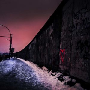 The Wall by David Drebin, a stone wall with a red heart graffiti and water washing against it