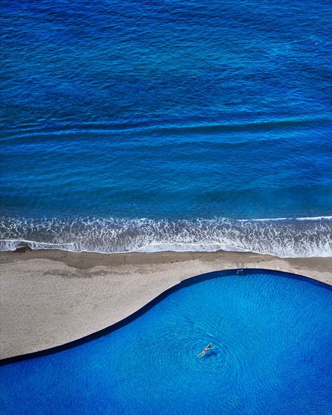 Blue Dream by David Drebin, model floating in organic shaped swimmingpool right next to the ocean