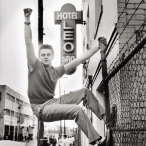Leonardo Di Caprio, Los Angeles by Mark Seliger, tha actor climbing a fence in front of a hotel sign