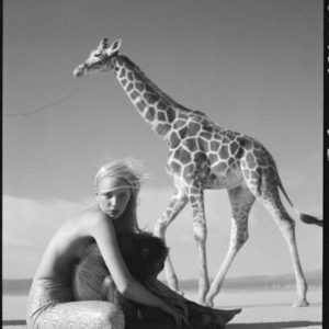 Beauty and Beast III by Michel Comte, Model sitting with monkey in the desert, a giraffe in the background