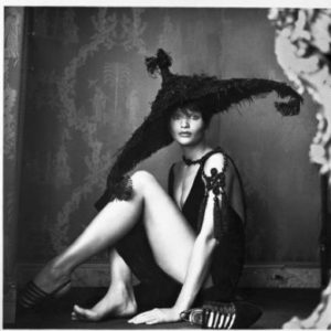 Helena Christensen with Hat by Michel Comte, the model sitting on the floor in a black dress and giant black hat
