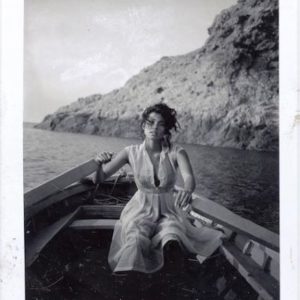 Claudia S. Corsica 1987, model in white dress in a rowingboad, cliffs in the background