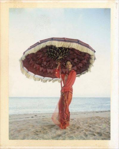 Leticia H. for L'Officiel Bali by Bruno Bisang, model in red dress standing on a beach and holding a purple parasol