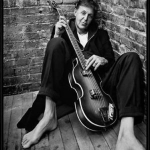 Paul McCartney by Mark Seliger, the musician leaning at a brick wall holding a guitar