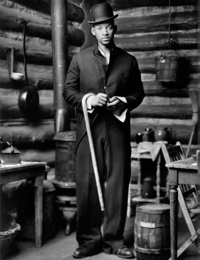 Will Smith, Big Sky Ranch, CA, 1997 by Mark Seliger, the actor in an oversized suit and tophat, carrying a cane in a loghouse kitchen