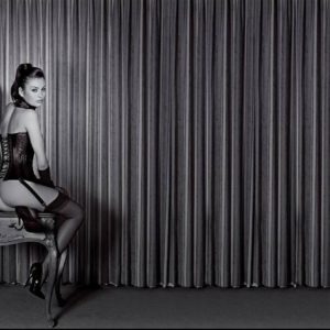 Petra in a leather Corset by Guido Argentini, model in corset and stockings sitting on an antique table in fron of a curtain