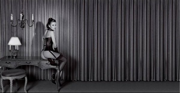 Petra in a leather Corset by Guido Argentini, model in corset and stockings sitting on an antique table in fron of a curtain