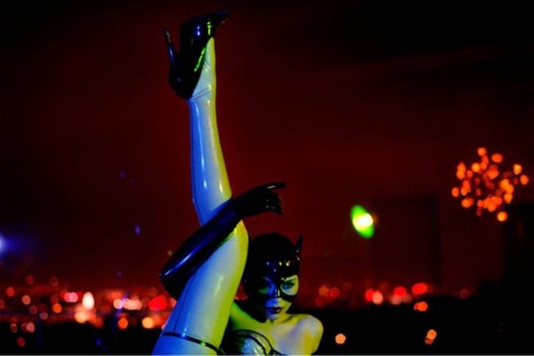 Thea as a cat by guido Argentini, model in latex dessous, illuminated in green and blue lights in front of red city lights