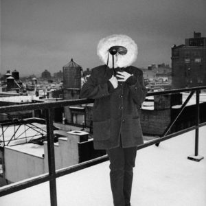 Cindy Sherman - New York 1995 by Albert Watson, the artist in a black suit and black and white ruffle mask on a snowy rooftop