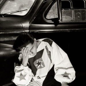 Man and Khrushchevs Hunting Limousine - Moscow 1988 by Albert Watson, man in white onepiece with stars and the udssr symbol in it sitting in front of an oldtimer car