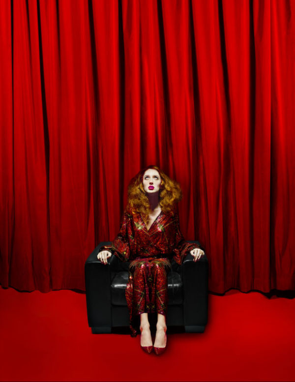 Teddy Quinlivan - Numero Berlin Magazine - NYC 2018 by Albert Watson, the british model in a red sequin jumber, sitting on a black leather armchair in front of red curtains and a red carpet