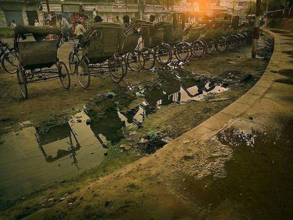 Street Scene Varanasi by Andreas H. Bitesnich, bike taxis lined up on a dirty road next to a puddle