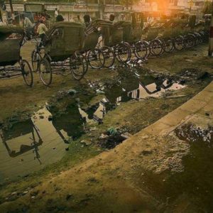 Street Scene Varanasi by Andreas H. Bitesnich, bike taxis lined up on a dirty road next to a puddle