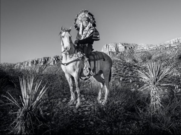 Apache by David Yarrow, a native american in feather headdress on a horse in the north american nature
